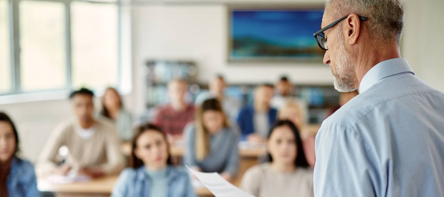a senior Caucasian male teacher in front of a high school classroom