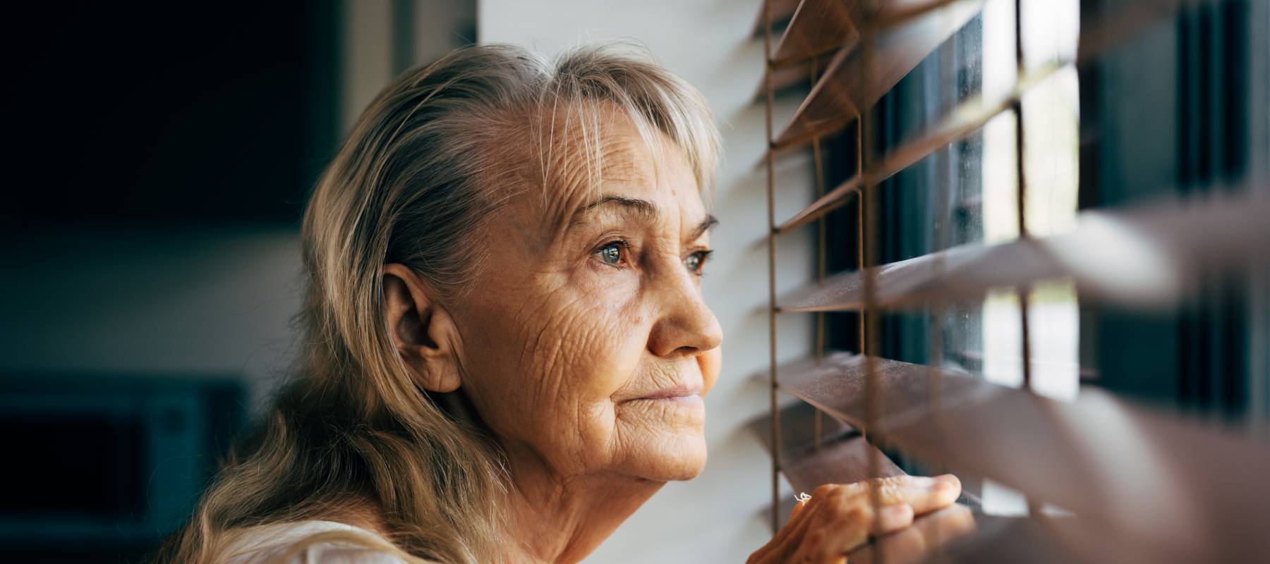 a senior Caucasian woman suspiciously looking outside her blinds