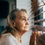 a senior Caucasian woman suspiciously looking outside her blinds