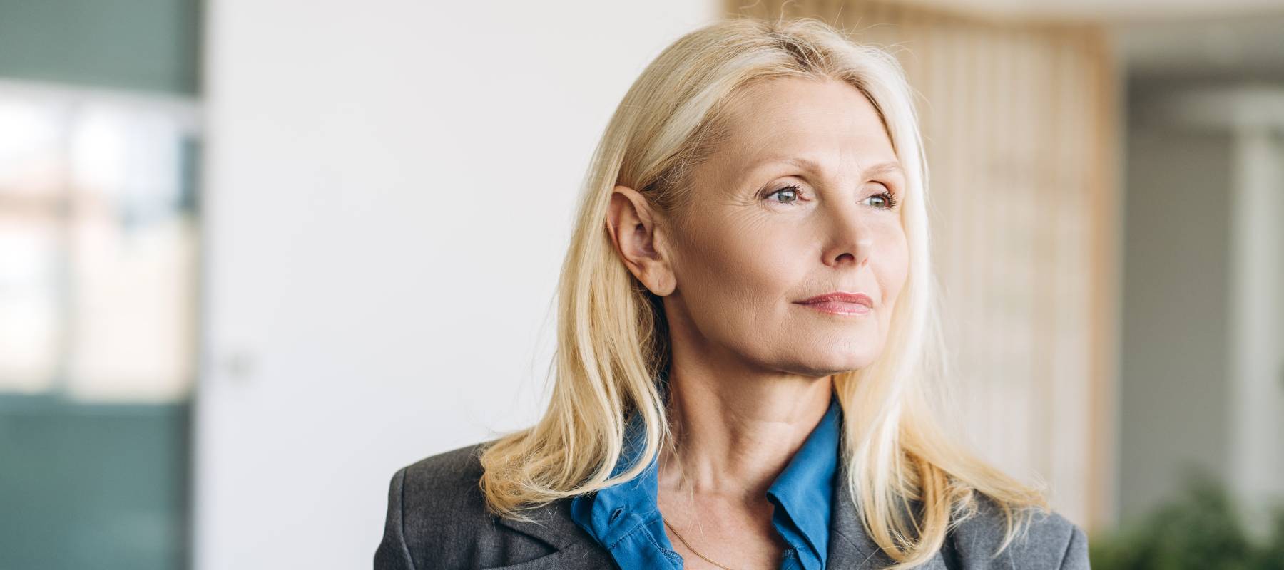 blonde Caucasian bsinesswoman looking away and thinking in office hallway