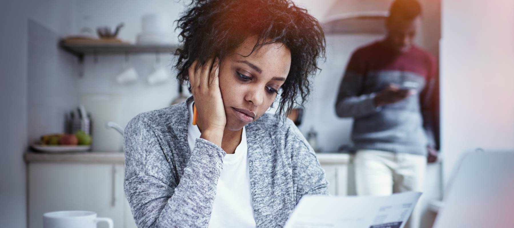 a young Black woman at her kitchen table, looking concerned over a stack of bills
