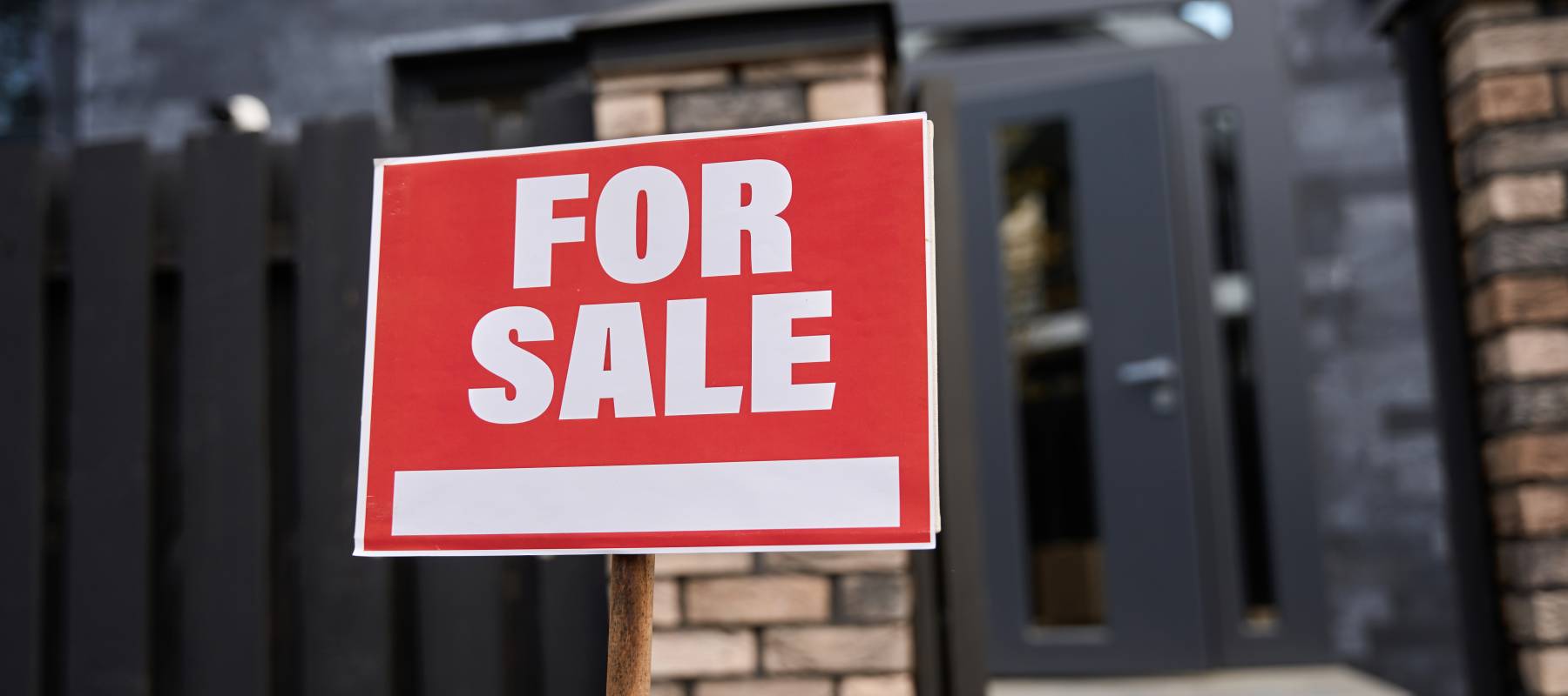 a red For Sale sign outside a black brick house