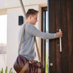 Young fashion designer busy closing his large wooden front door of his beautiful beach house with several plants planted along side the entrance