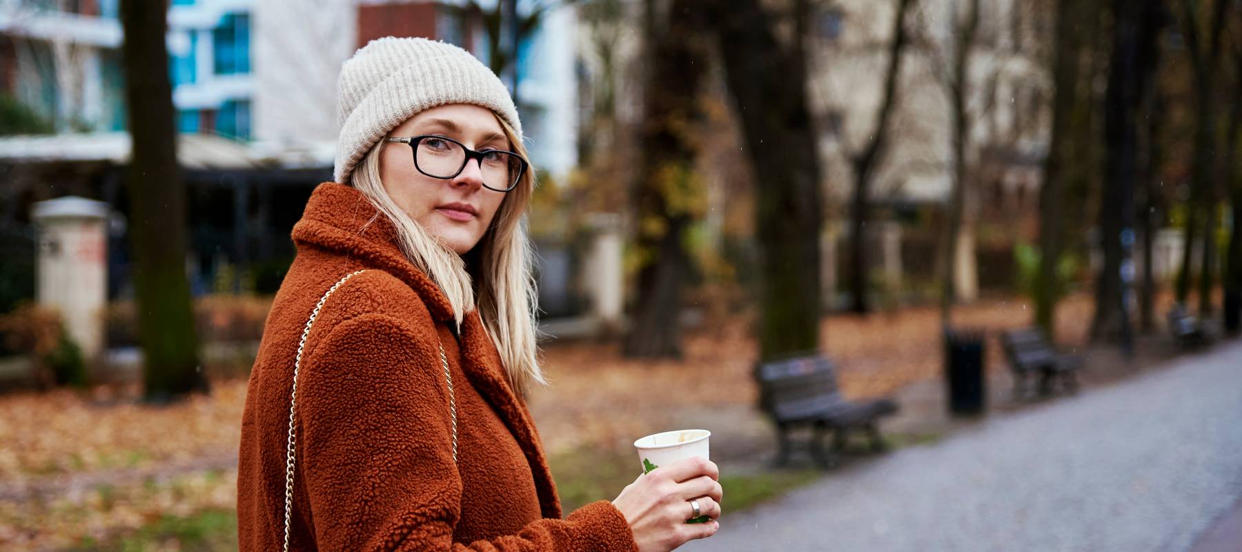 a blonde woman holding a coffee and going for a walk in the city