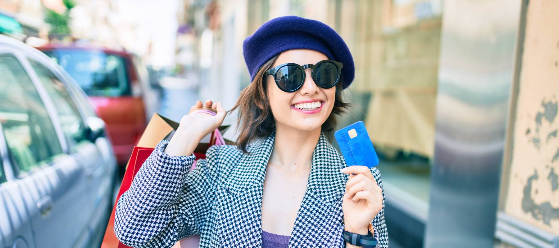 a young Caucasian woman walking down a city street with a credit card and shopping bags