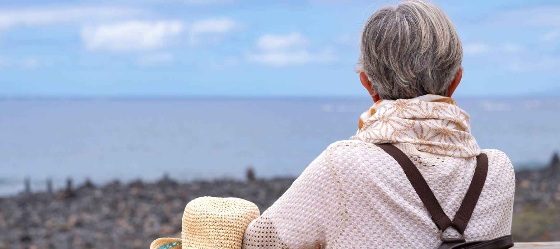 A senior woman with a backpack looks toward the sea's horizon.