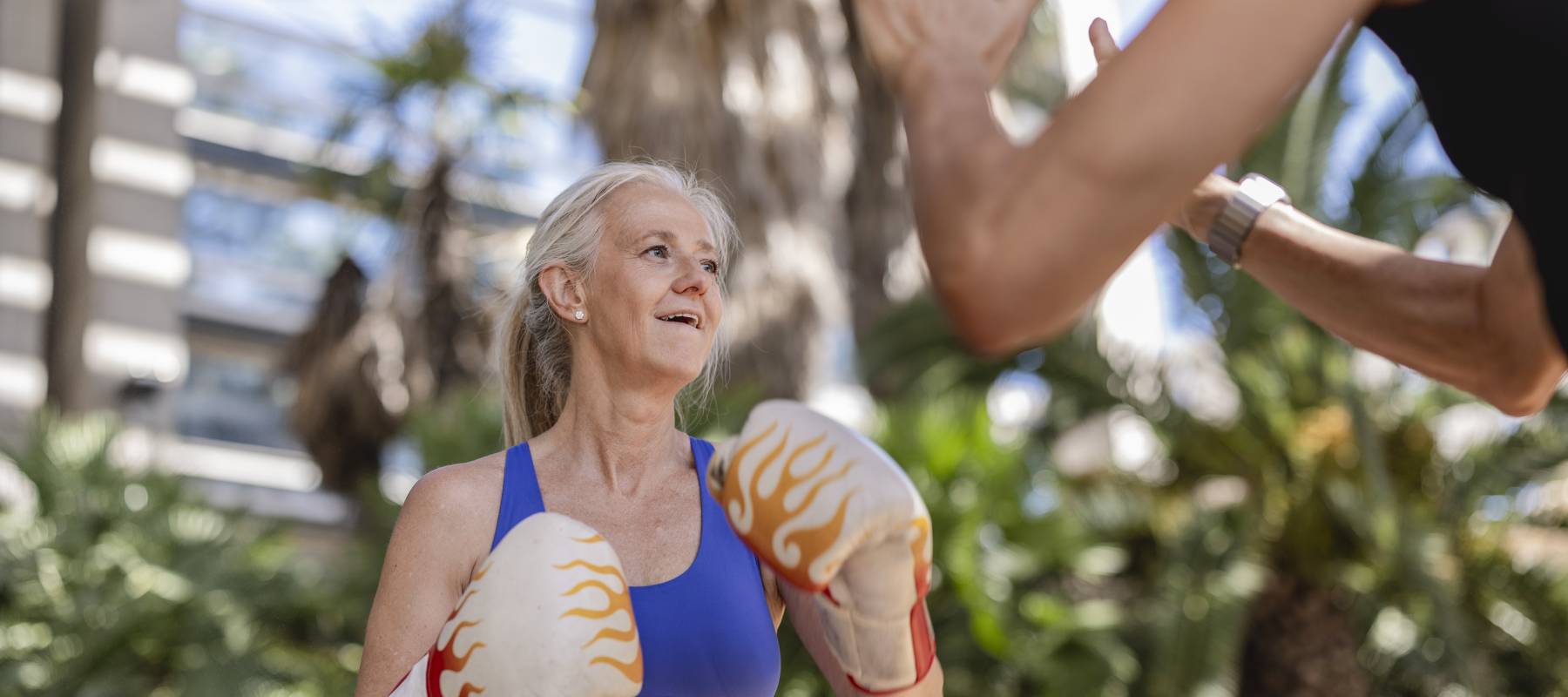 senior Caucasian woman boxing with personal trainer outdoors, active lifestyle and fitness motivation