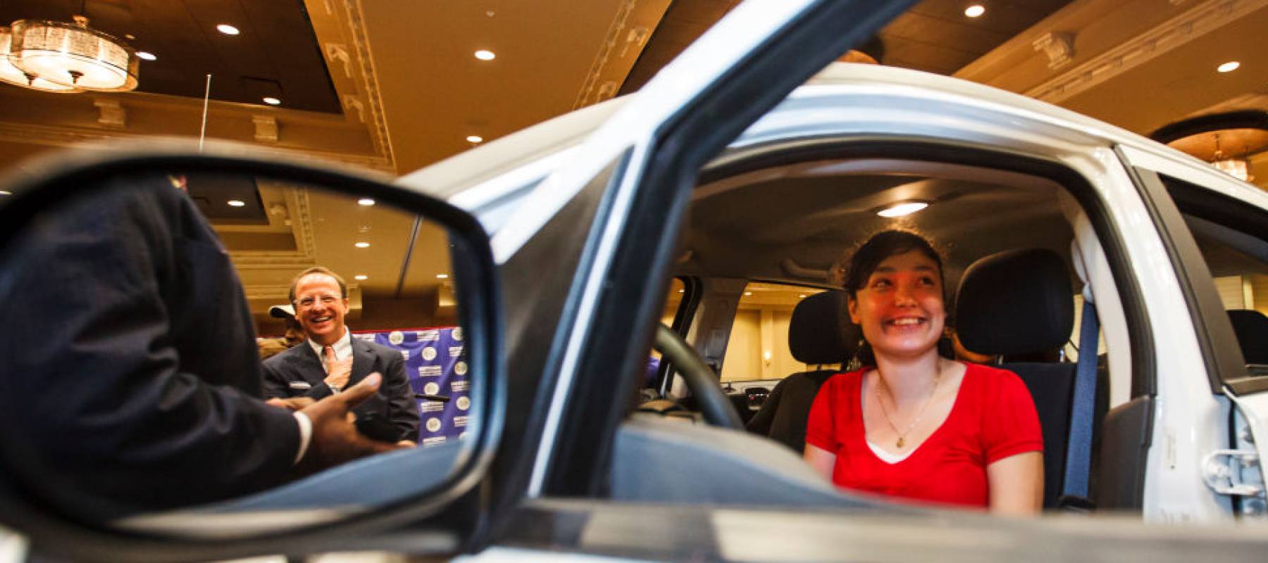 A woman sits in a car at a dealership.