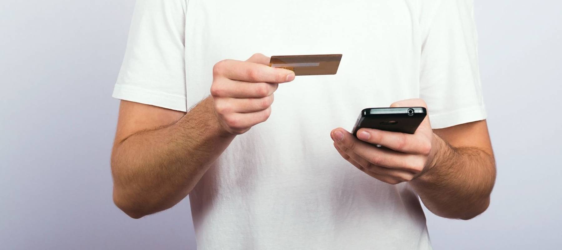 Portrait of a guy who holds a credit card and pays a mobile payment