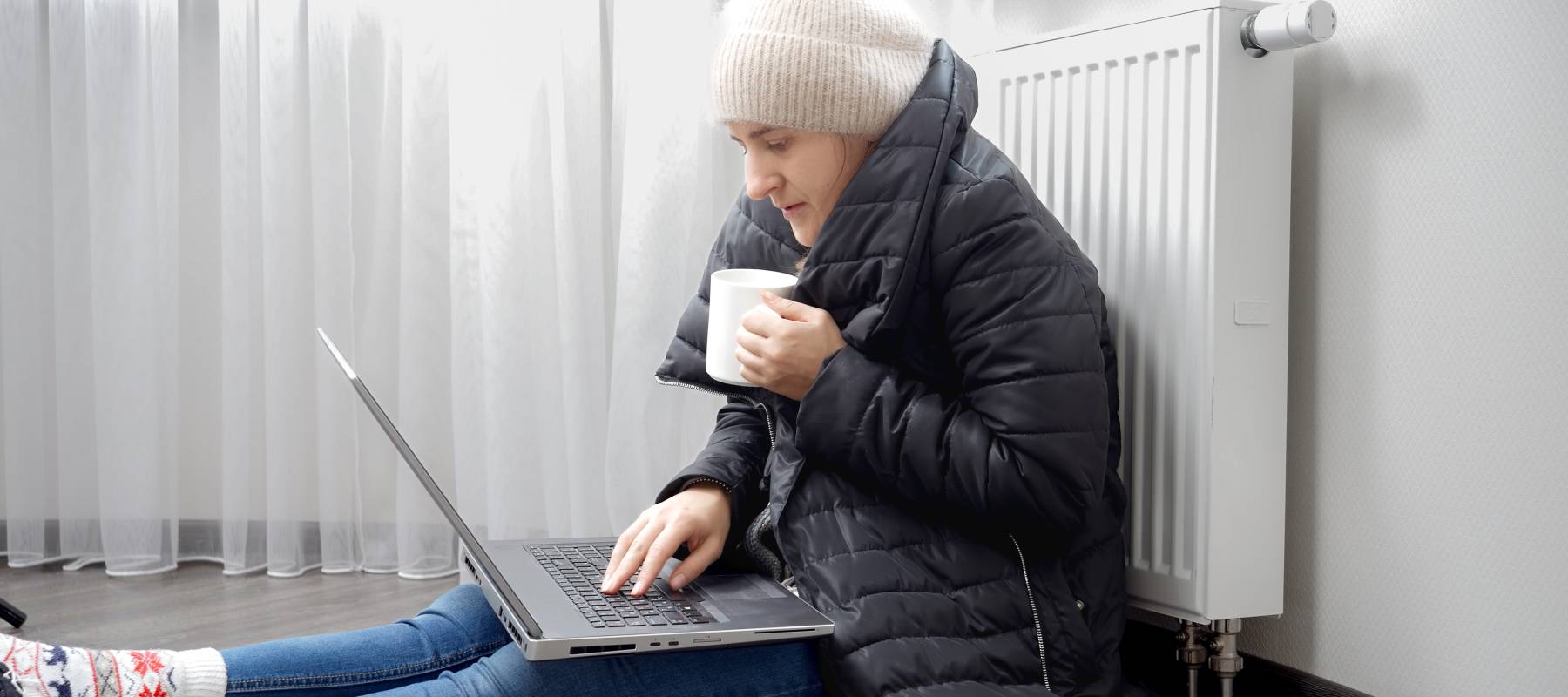 Woman works on computer indoors next to radiator with coat on