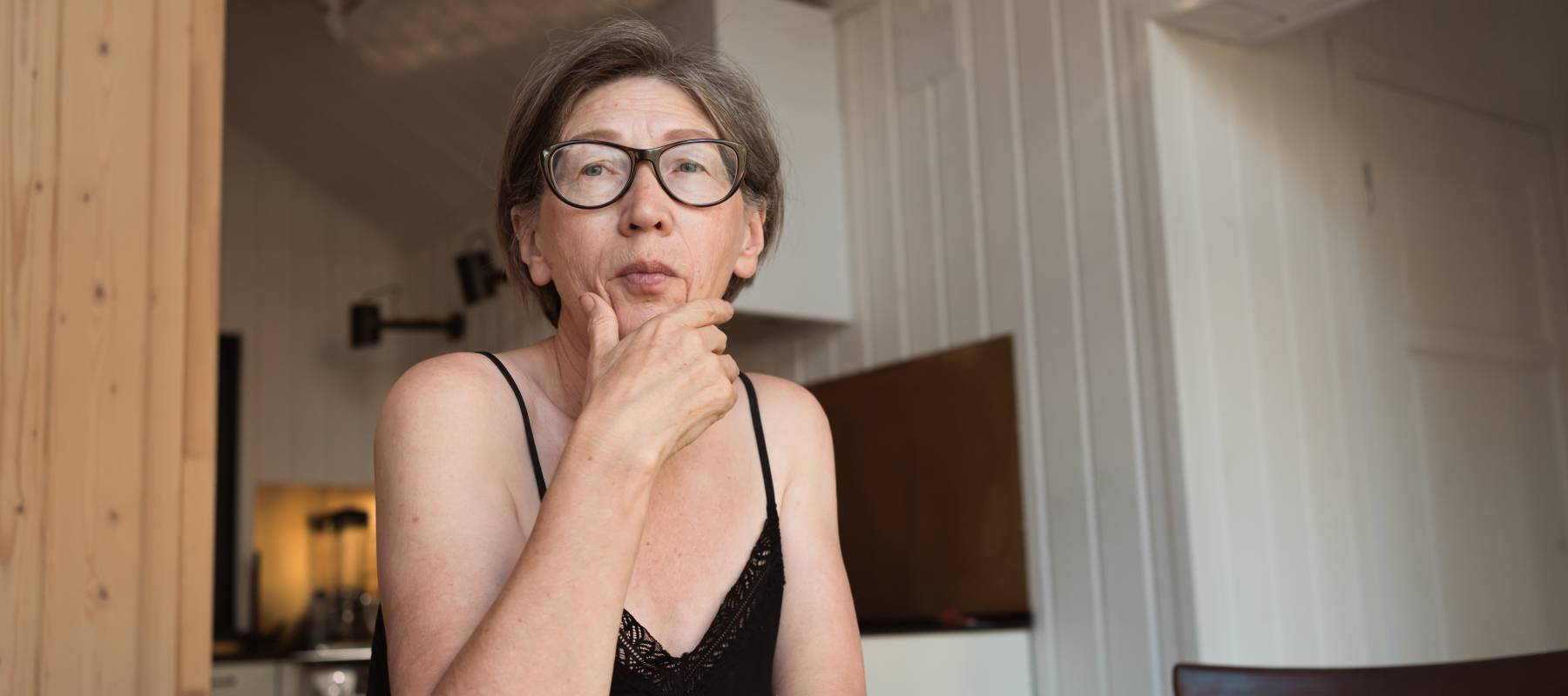 worried senior 60s woman wearing glasses sitting at the kitchen table