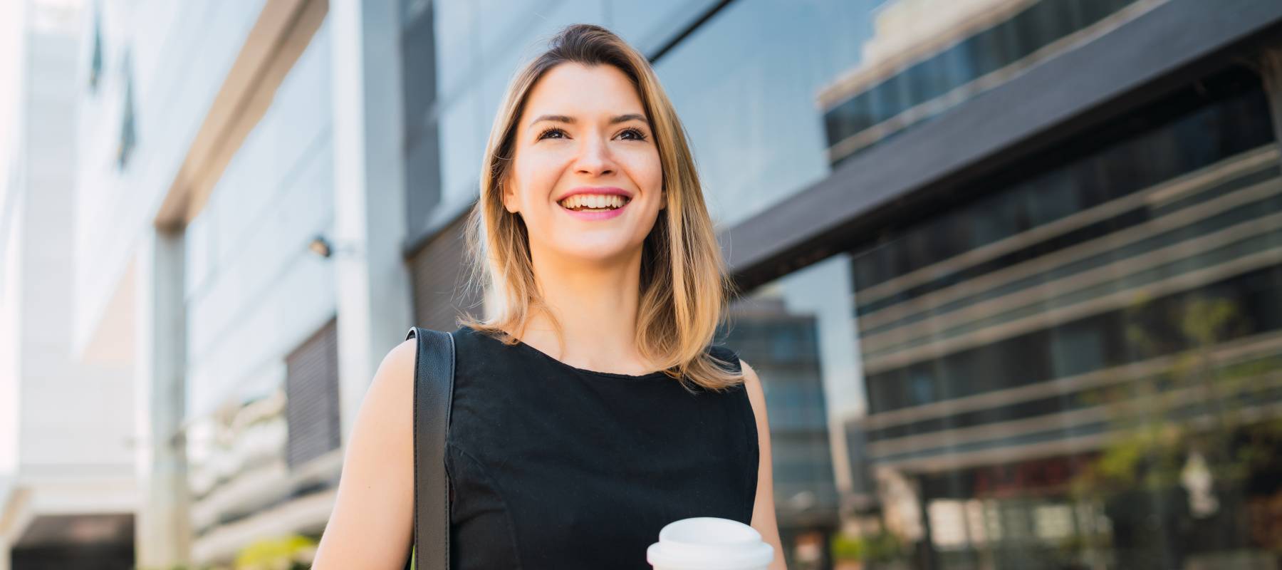 young professional Caucasian woman smiling outside on her way to work with a coffee
