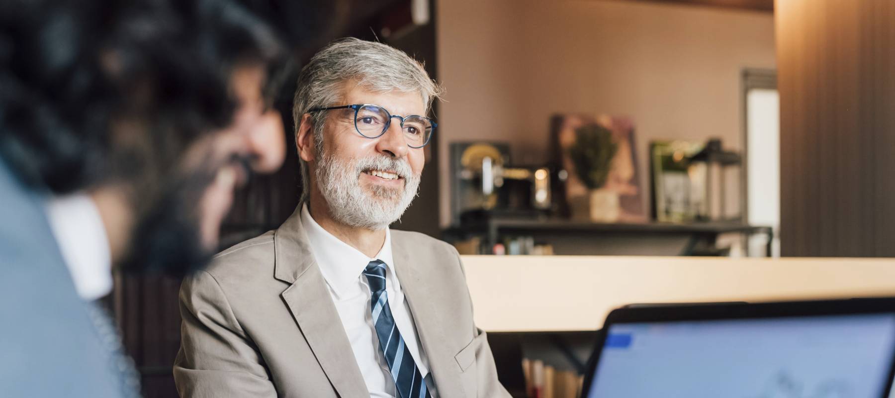 older Caucasian man in a meeting with an open laptop