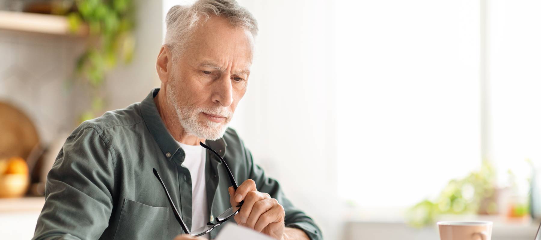 senior Caucasian man reviewing documents while sitting at kitchen desk