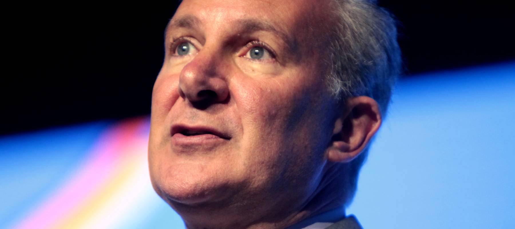 Peter Schiff speaks at an event in a tan suit and white shirt.