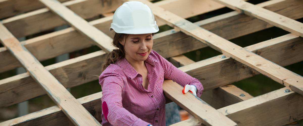 woman in hard hat standing on a ladder, staining some roof beams