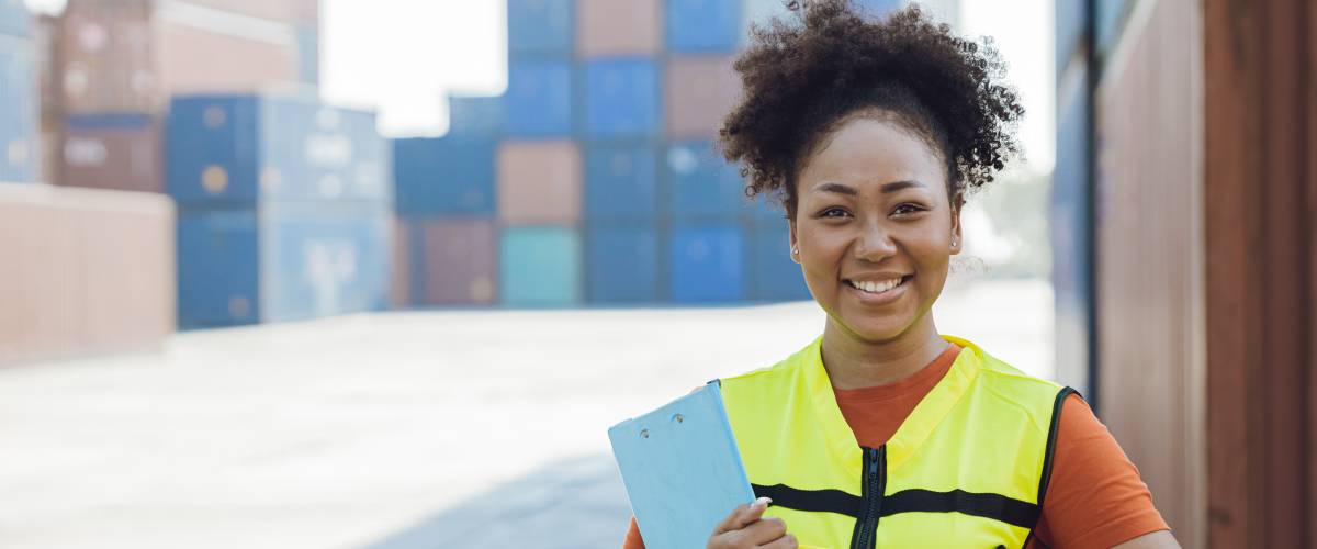 woman standing in front of shipping containers holding a yellow hardhat
