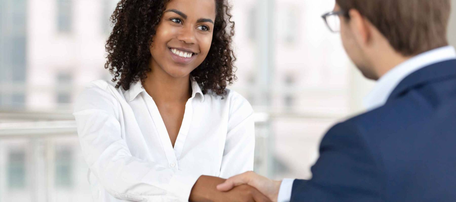 Smiling woman shakes hands with man in suit who has back to camera