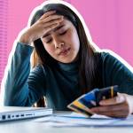 Close up of woman holding her head, looking at multiple credit cards in her hand