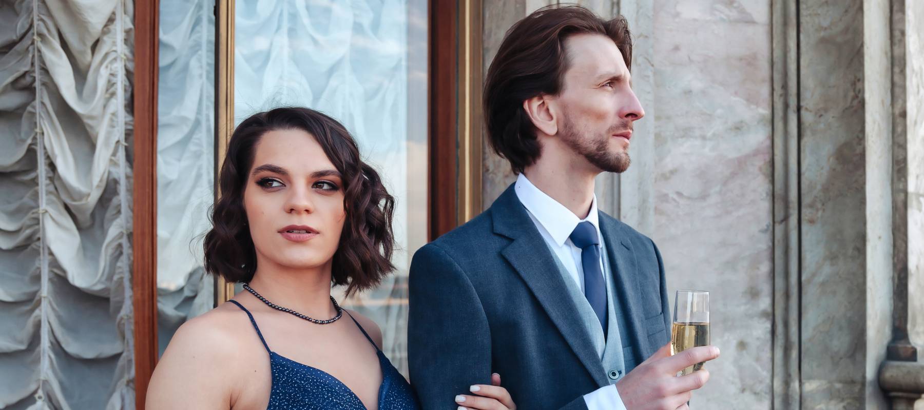 A wealthy young couple pose outside a mansion.