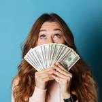 Woman holds fanned out American cash in her hands in front of her face