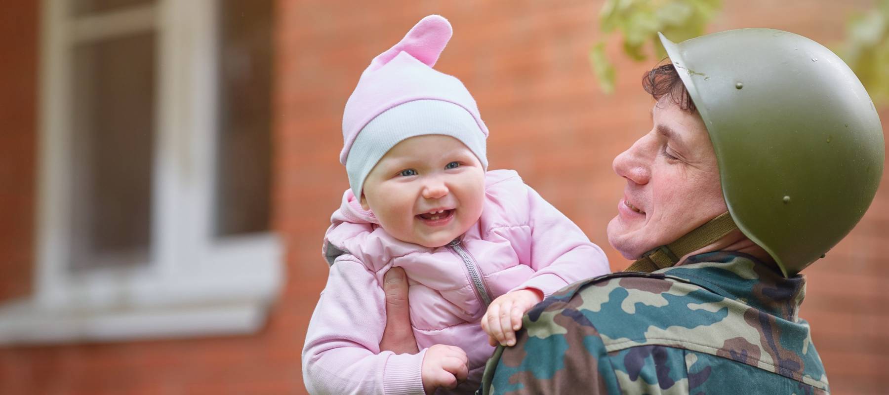 Military man in a helmet with a smiling little baby in his arms.