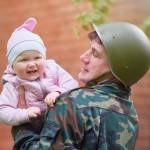 Military man in a helmet with a smiling little baby in his arms.