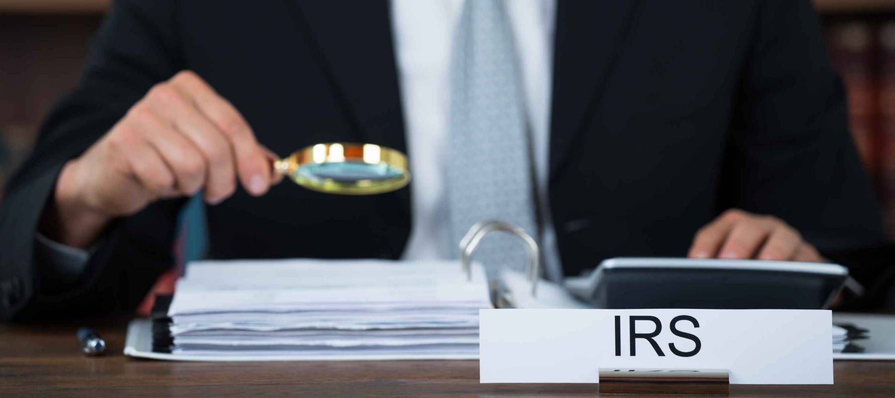 Midsection of tax auditor examining documents with magnifying glass at table in office