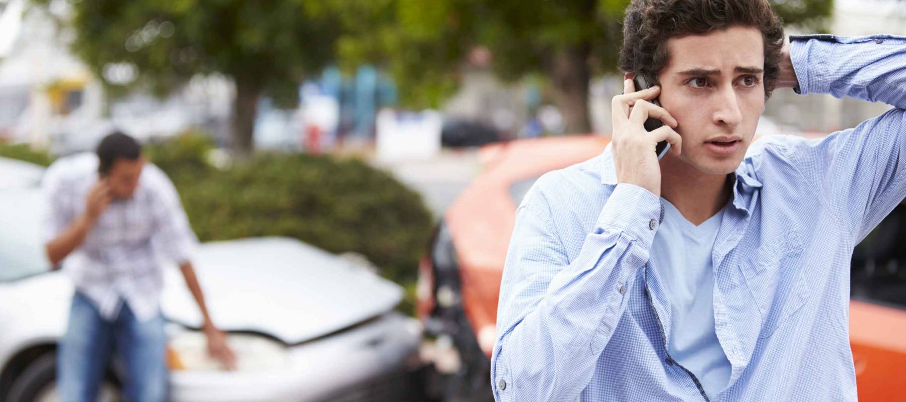 Young man making phone call with car accident in background