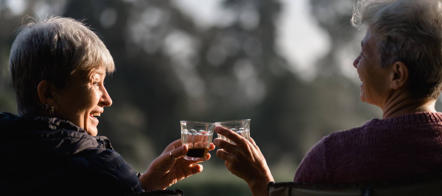 Two older women clink glasses outside.