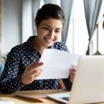 Smiling young woman holding paper while sitting in front of a laptop,
