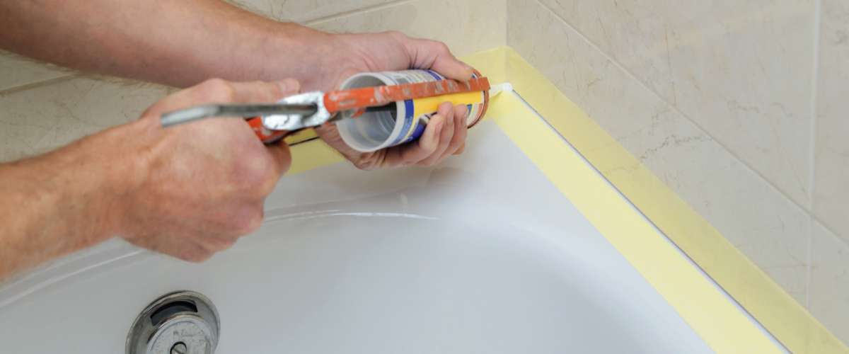 Worker puts silicone sealant to caulk the joint between tub and wall