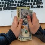 Man holding cash in front of a laptop