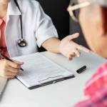 Close up of doctor talking to man across the table while filling out a form