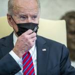 President Joe Biden wearing a mask holding a pen during conversation with staff and media