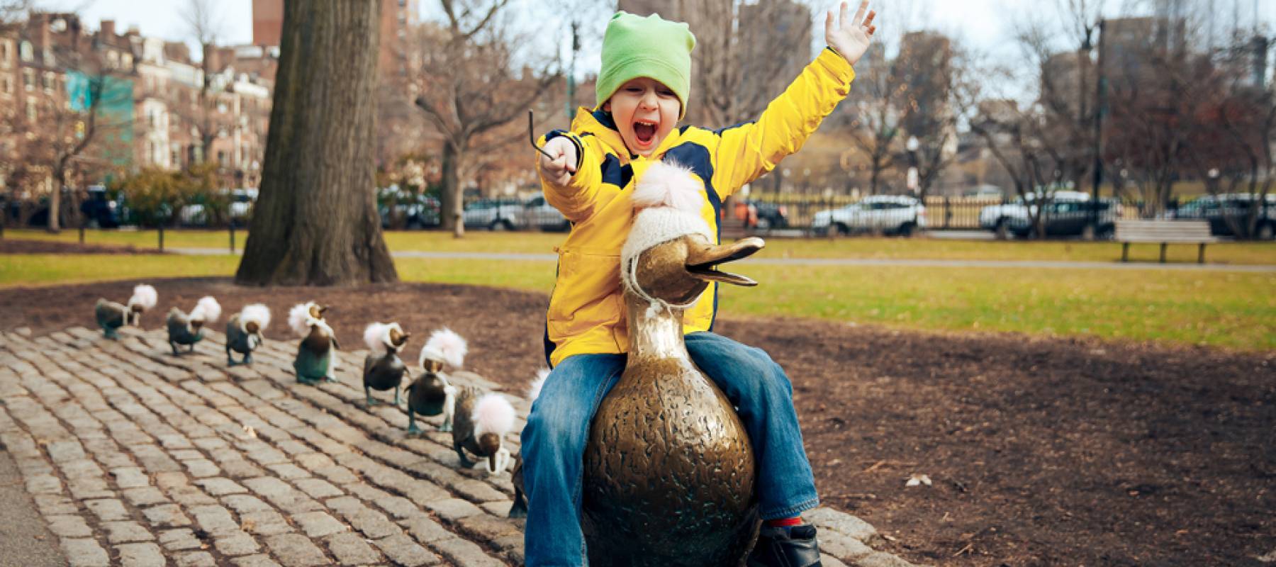 A boy riding a duck sculpture in Boston Public Garden.