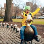 A boy riding a duck sculpture in Boston Public Garden.