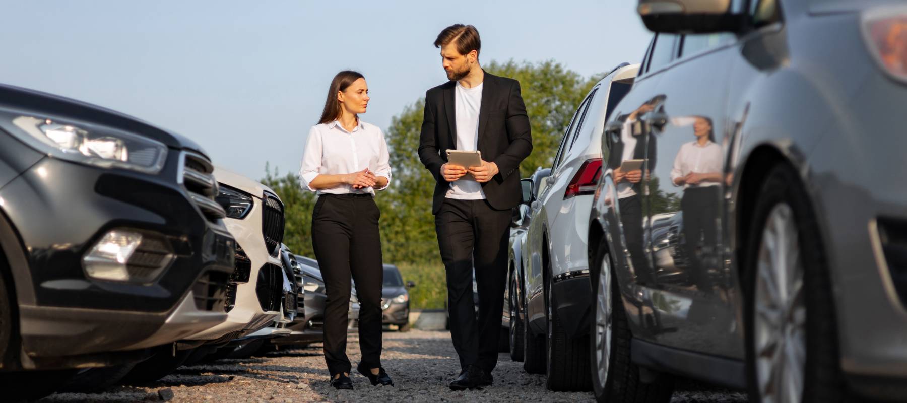 A salesperson and customer walk through a car dealership lot.