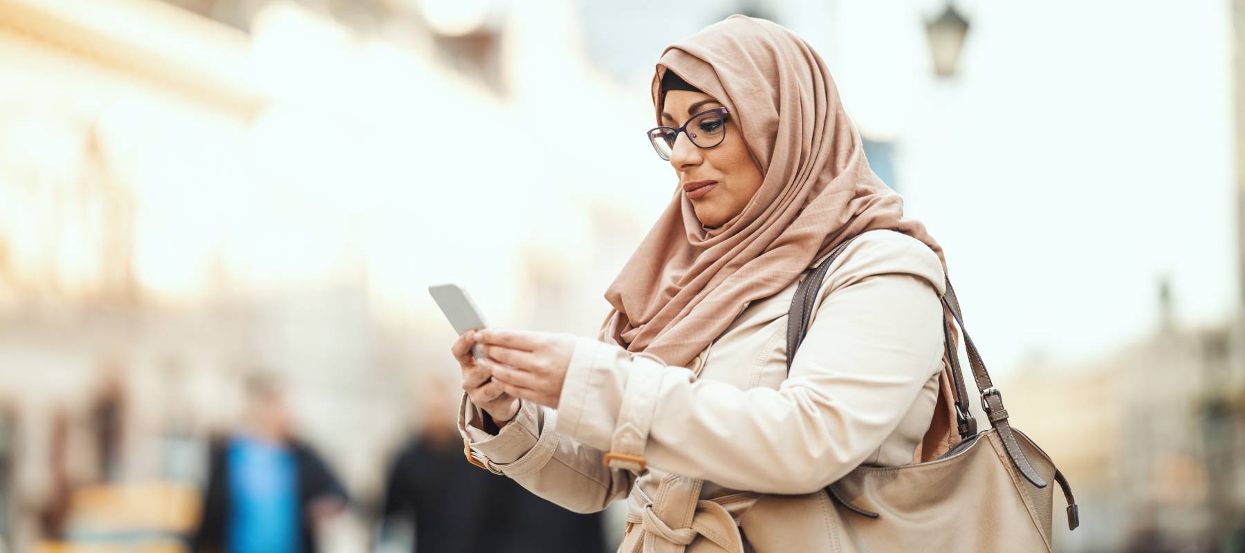 A woman wearing a hijab sends money abroad on her phone.