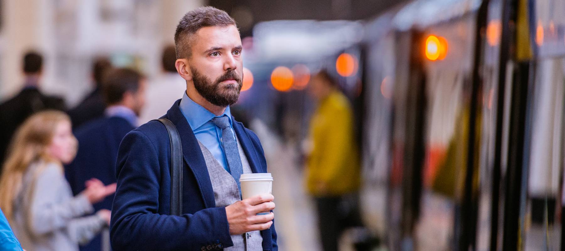 A businessman holding a large coffee while waiting to board a commuter train..