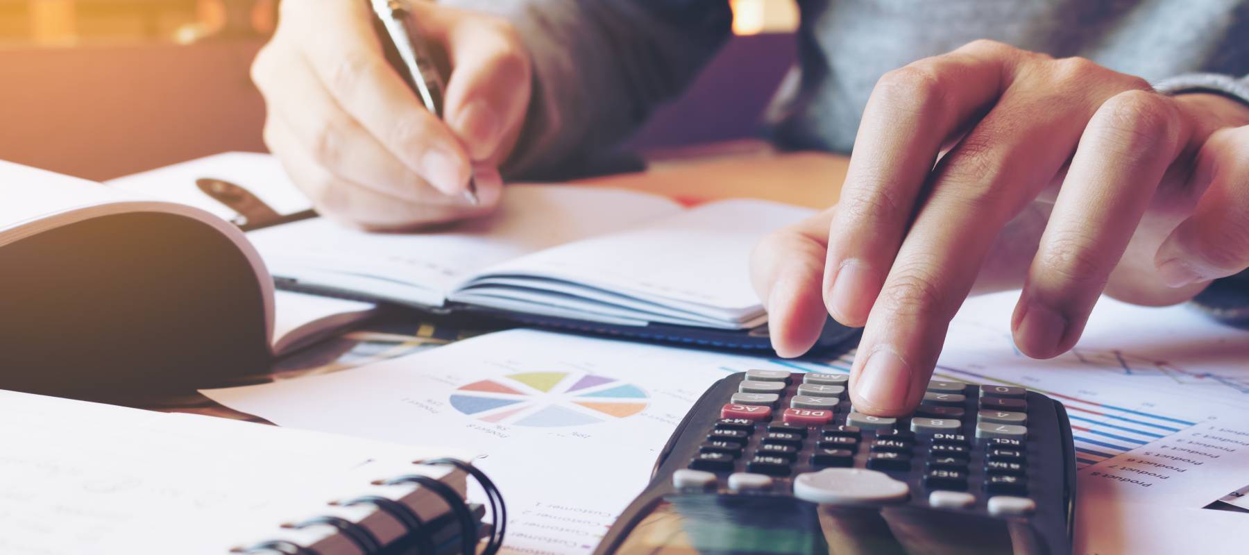 A person using a calculator and writing notes on a desk.