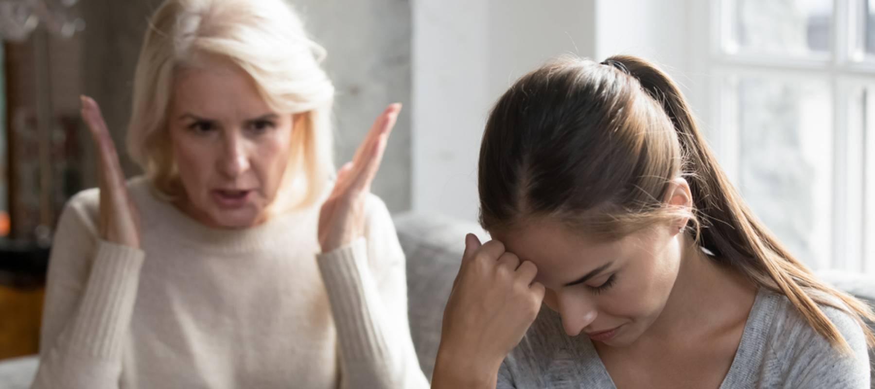 Mid aged mother sit on couch scold grown up daughter.