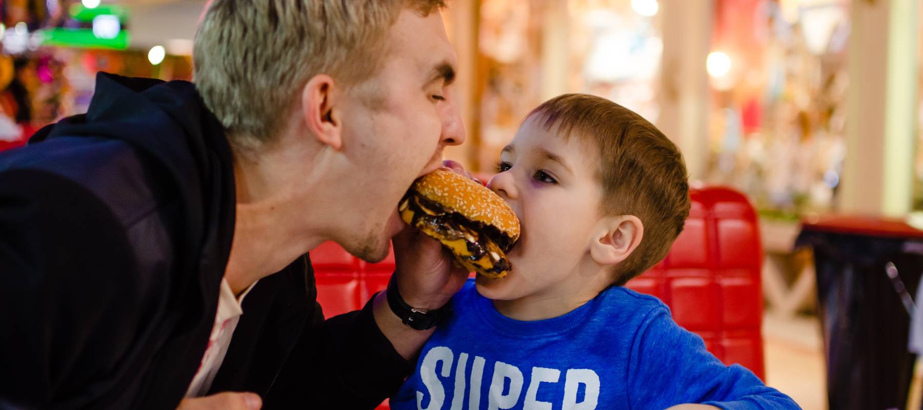 A father and son, at a fast-food restaurant, share a burger.
