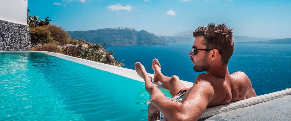 man relaxing in infinity swimming pool looking at the ocean,young man in the swimming pool relaxing looking out over the ocen caldera of Oia Santorini Greece