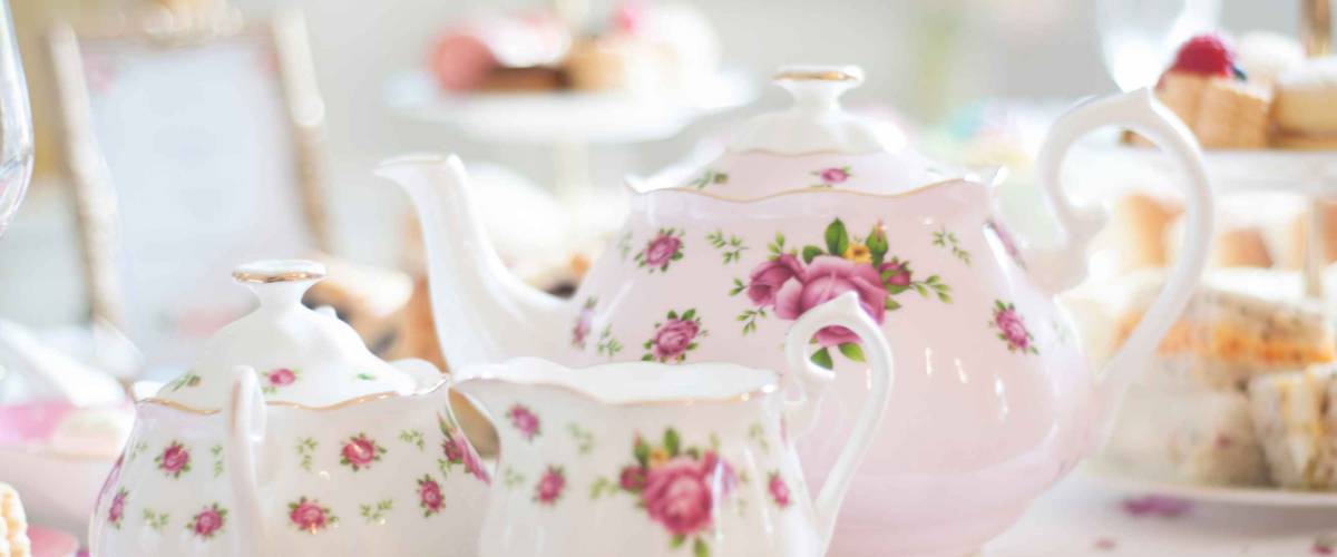 Close up of pastel pink Royal Doulton teapot and tea set for an elegant high tea party table set up an assortment of cupcakes, sweets and pastries.