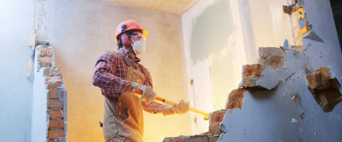 worker with sledgehammer at indoor wall destroying