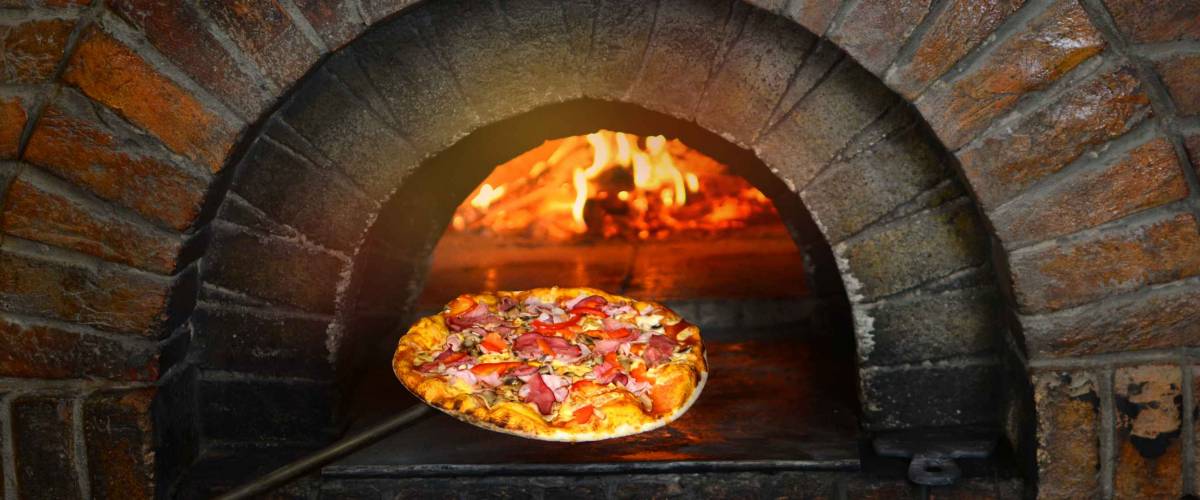 Pizza near the stone stove with fire. Background of a traditional pizzeria restaurant with a fire place.