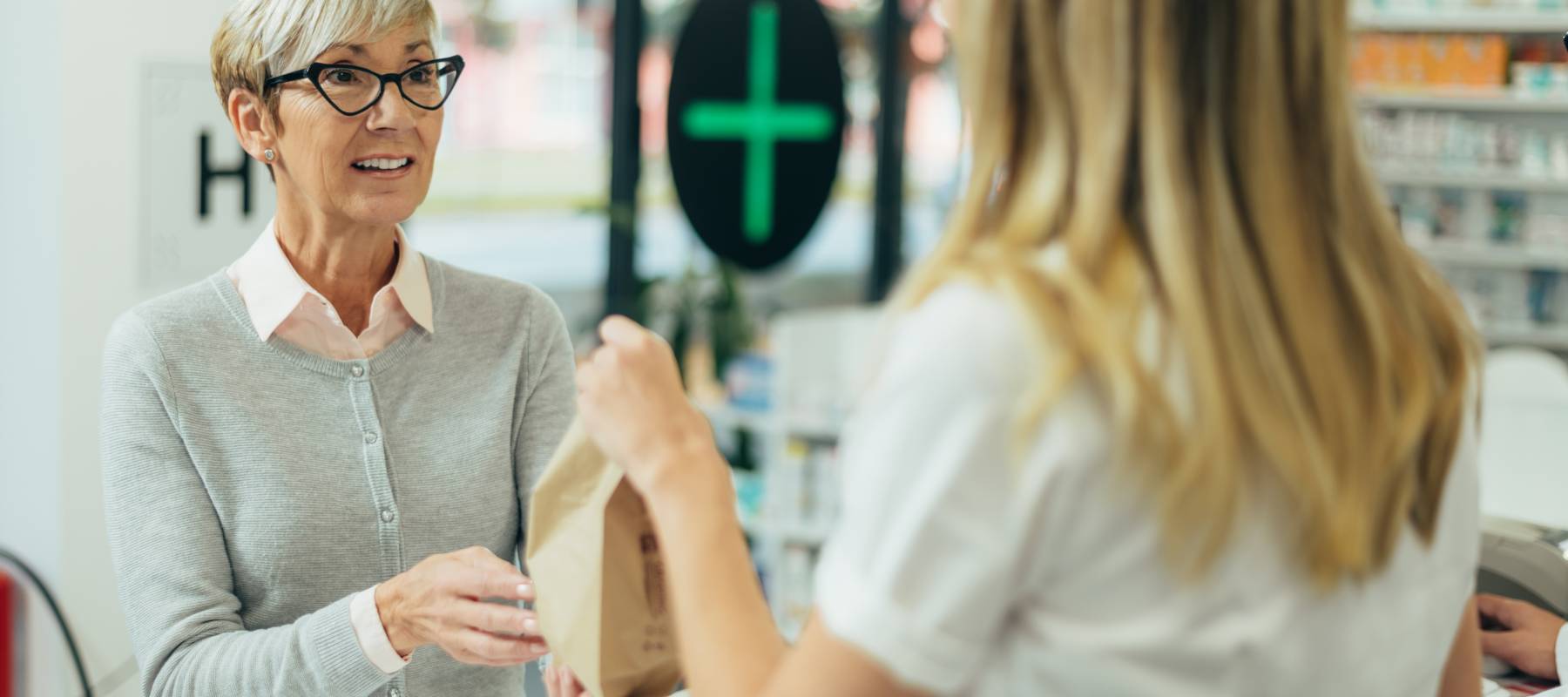 A woman, with a surprised expression, picks up a prescription from a pharmacy.