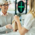 A woman, with a surprised expression, picks up a prescription from a pharmacy.