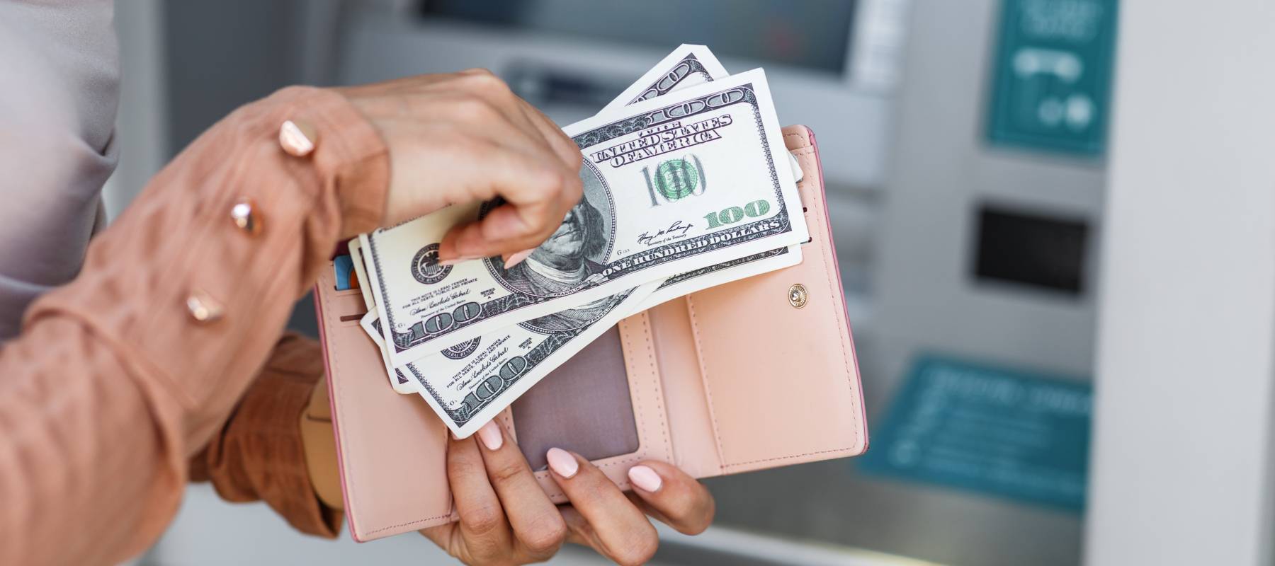A close-up of a woman with bright pink nails sorting bills from an ATM.
